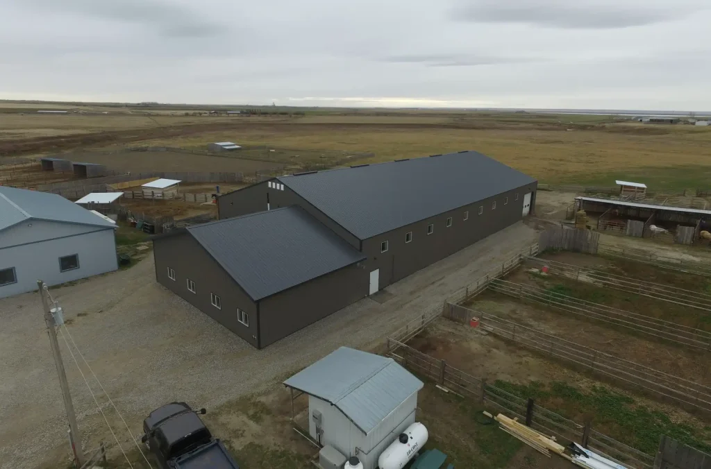 A sable post-frame riding arena with overhead doors, an open lean-to and kickwall