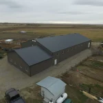 A sable post-frame riding arena with overhead doors, an open lean-to and kickwall