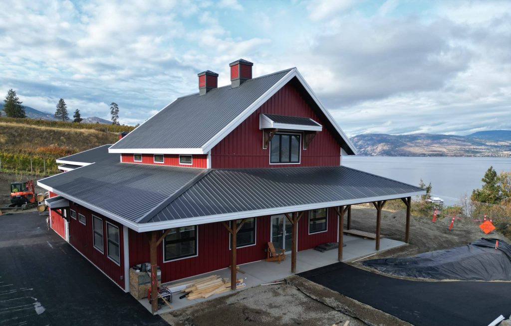 A dark red post-frame barndominium with cupolas, attached garage with overhead doors, open lean-tos, soffits, and timber accents