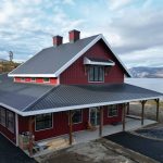 A dark red post-frame barndominium with cupolas, attached garage with overhead doors, open lean-tos, soffits, and timber accents