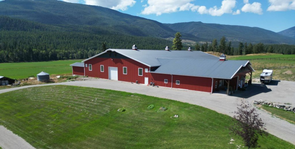 A tile red post-frame riding arena with overhead doors, timber accents, and soffits