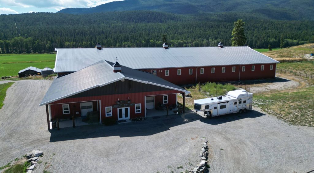 A tile red post-frame riding arena with overhead doors, timber accents, and soffits