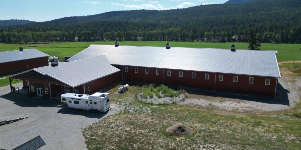 A tile red post-frame riding arena with overhead doors, timber accents, and soffits