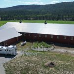 A tile red post-frame riding arena with overhead doors, timber accents, and soffits