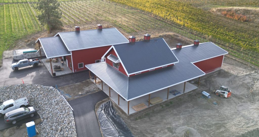 A dark red post-frame barndominium with cupolas, attached garage with overhead doors, open lean-tos, soffits, and timber accents