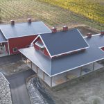 A dark red post-frame barndominium with cupolas, attached garage with overhead doors, open lean-tos, soffits, and timber accents