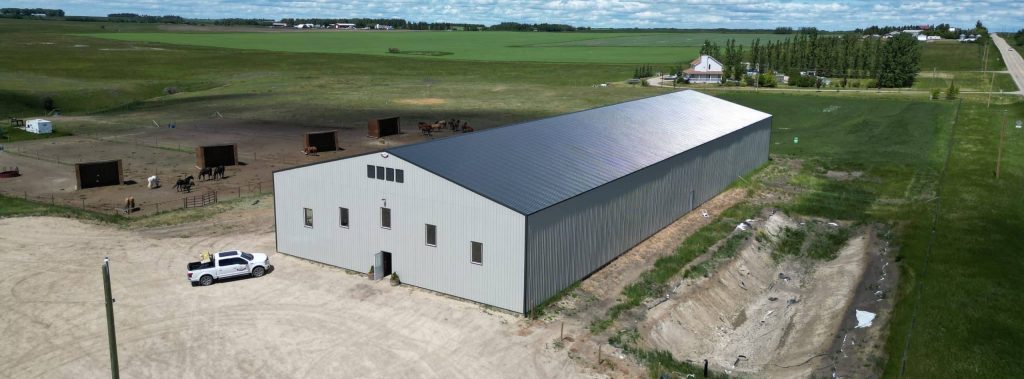 A stone grey post-frame riding arena with three overhead doors