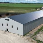 A stone grey post-frame riding arena with three overhead doors
