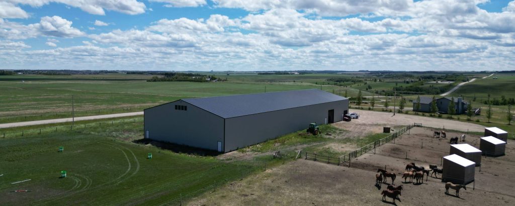A stone grey post-frame riding arena with three overhead doors