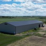 A stone grey post-frame riding arena with three overhead doors