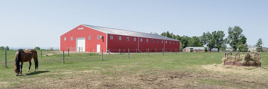 A bright red post-frame riding arena with overhead doors