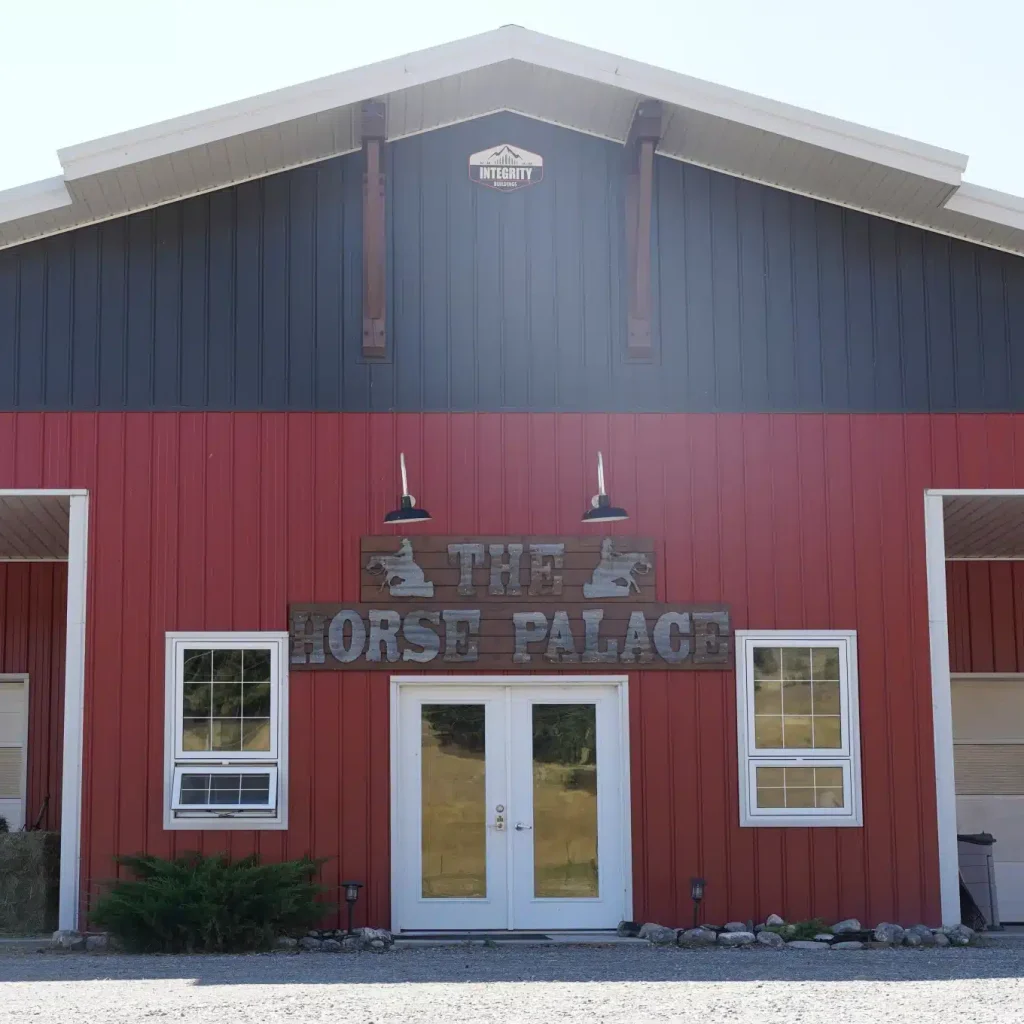 A tile red post-frame riding arena with overhead doors, timber accents, and soffits