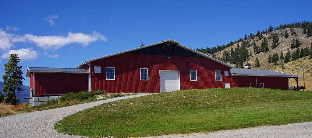 A tile red post-frame riding arena with overhead doors, timber accents, and soffits