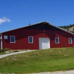 A tile red post-frame riding arena with overhead doors, timber accents, and soffits