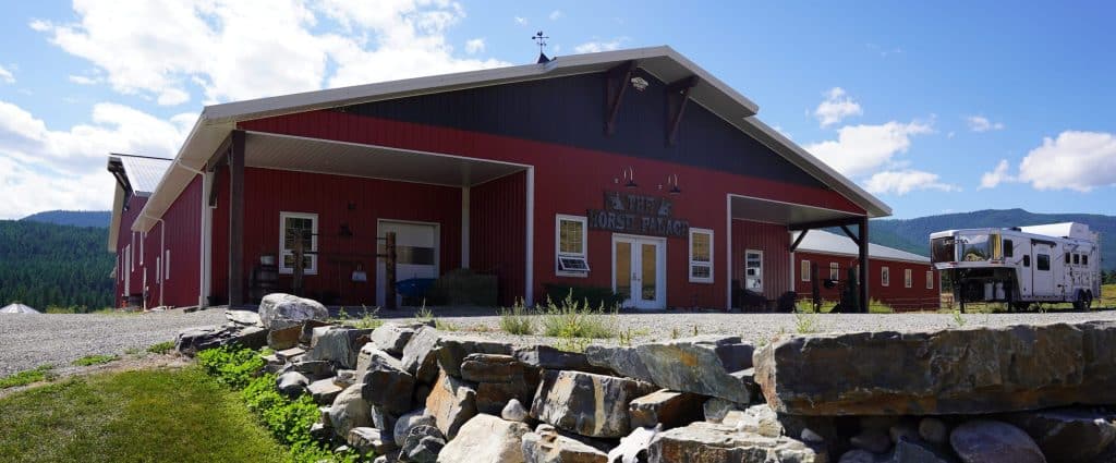 A tile red post-frame riding arena with overhead doors, timber accents, and soffits