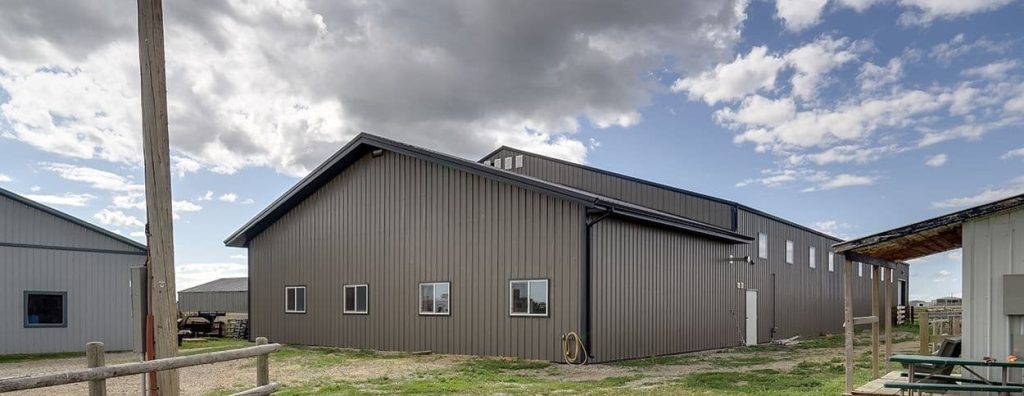 A sable post-frame riding arena with overhead doors, an open lean-to and kickwall