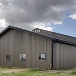 A sable post-frame riding arena with overhead doors, an open lean-to and kickwall