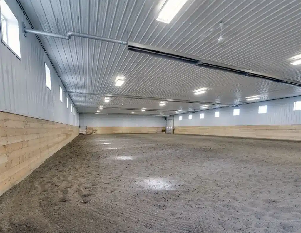 A sable post-frame riding arena with overhead doors, an open lean-to and kickwall