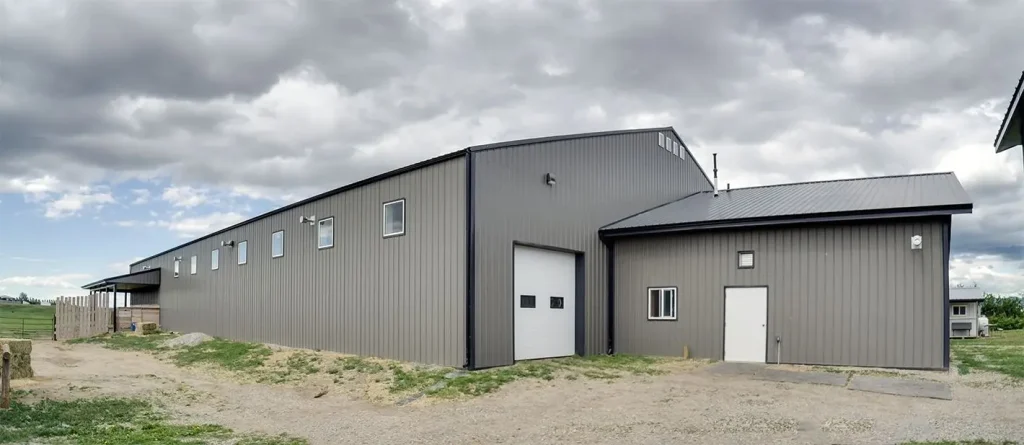 A sable post-frame riding arena with overhead doors, an open lean-to and kickwall