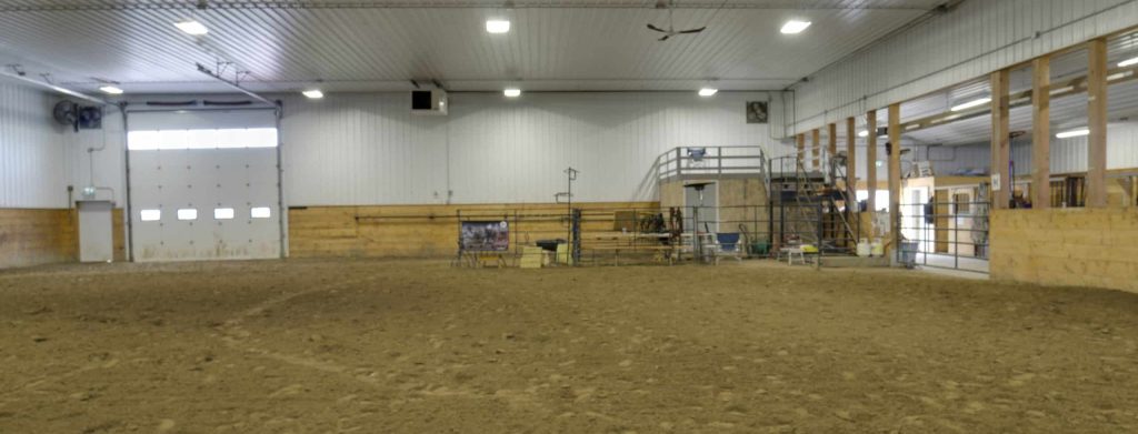 A stone grey post frame equestrian riding arena with attached barn