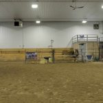 A stone grey post frame equestrian riding arena with attached barn