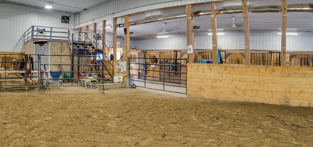 A stone grey post frame equestrian riding arena with attached barn