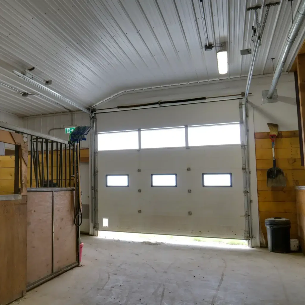 A stone grey post frame equestrian riding arena with attached barn