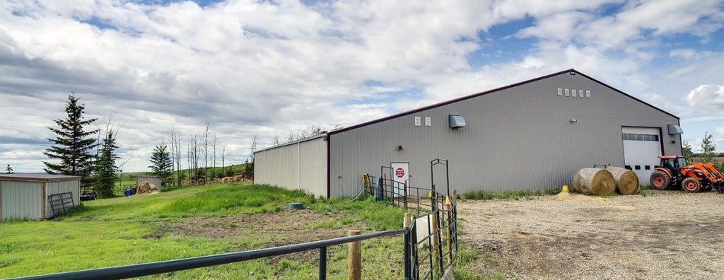 A stone grey post frame equestrian riding arena with attached barn