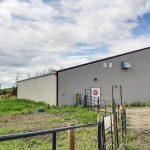 A stone grey post frame equestrian riding arena with attached barn