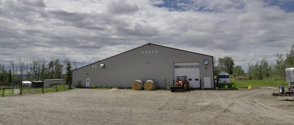 A stone grey post frame equestrian riding arena with attached barn