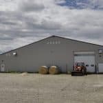 A stone grey post frame equestrian riding arena with attached barn