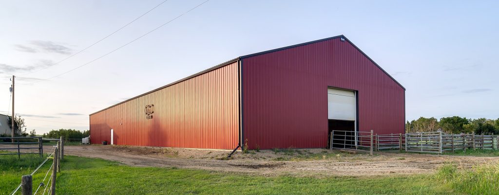 A dark red post-frame riding arena with a chain overhead door
