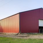 A dark red post-frame riding arena with a chain overhead door