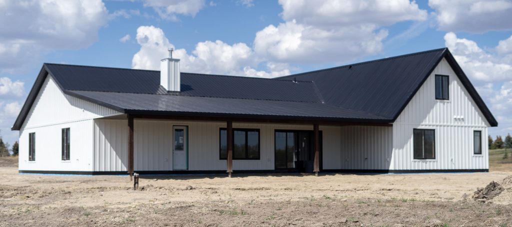 A white white post-frame Homestead with loft, with an overhead door, soffits, and timber accents