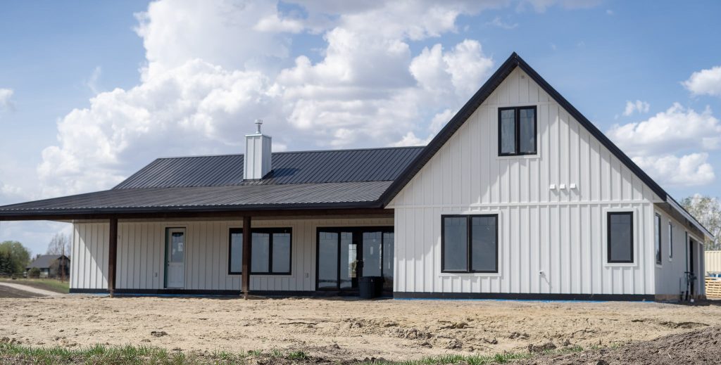 A white white post-frame Homestead with loft, with an overhead door, soffits, and timber accents