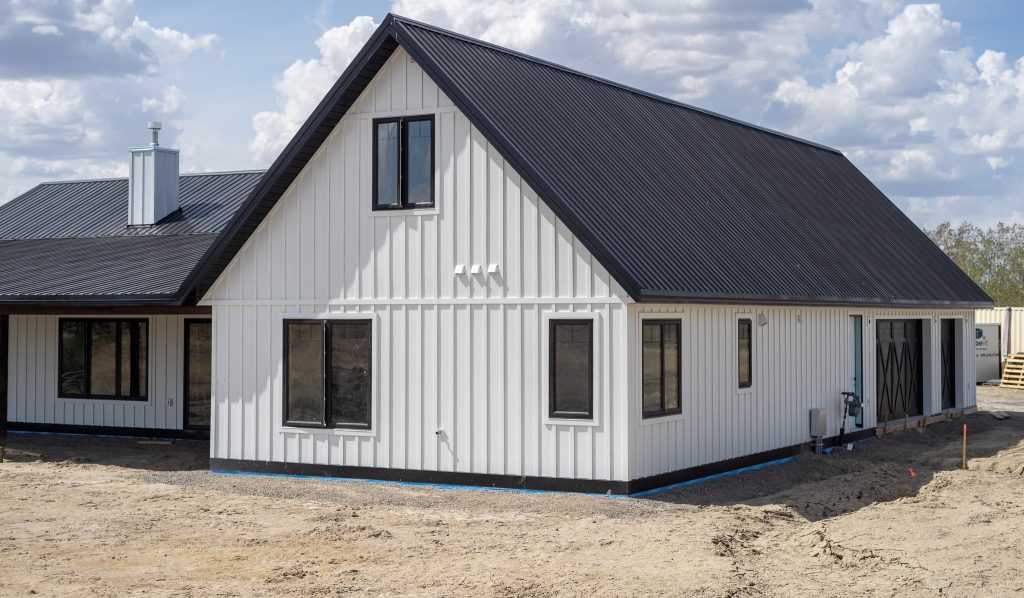 A white white post-frame Homestead with loft, with an overhead door, soffits, and timber accents