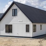 A white white post-frame Homestead with loft, with an overhead door, soffits, and timber accents