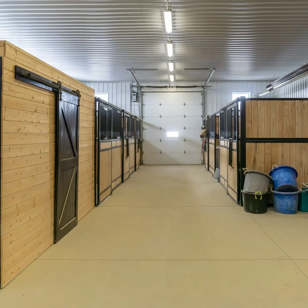 A dark red post-frame riding arena with soffits, sliding doors, and two overhead doors