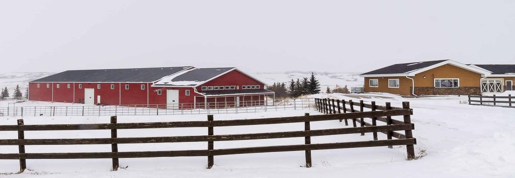 A dark red post-frame riding arena with soffits, sliding doors, and two overhead doors