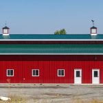 A dark red post-frame equestrian barn with a unique custom cupola