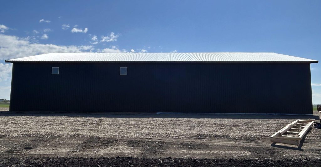 A black post-frame machine shed with a black bi-fold door and two overhead doors