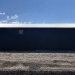A black post-frame machine shed with a black bi-fold door and two overhead doors