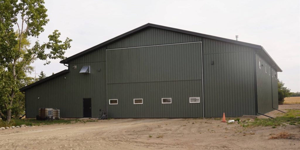 A Dark Sage post-frame agricultural shop with two overhead doors, a bi-fold door, an open and closed lean-to and soffits