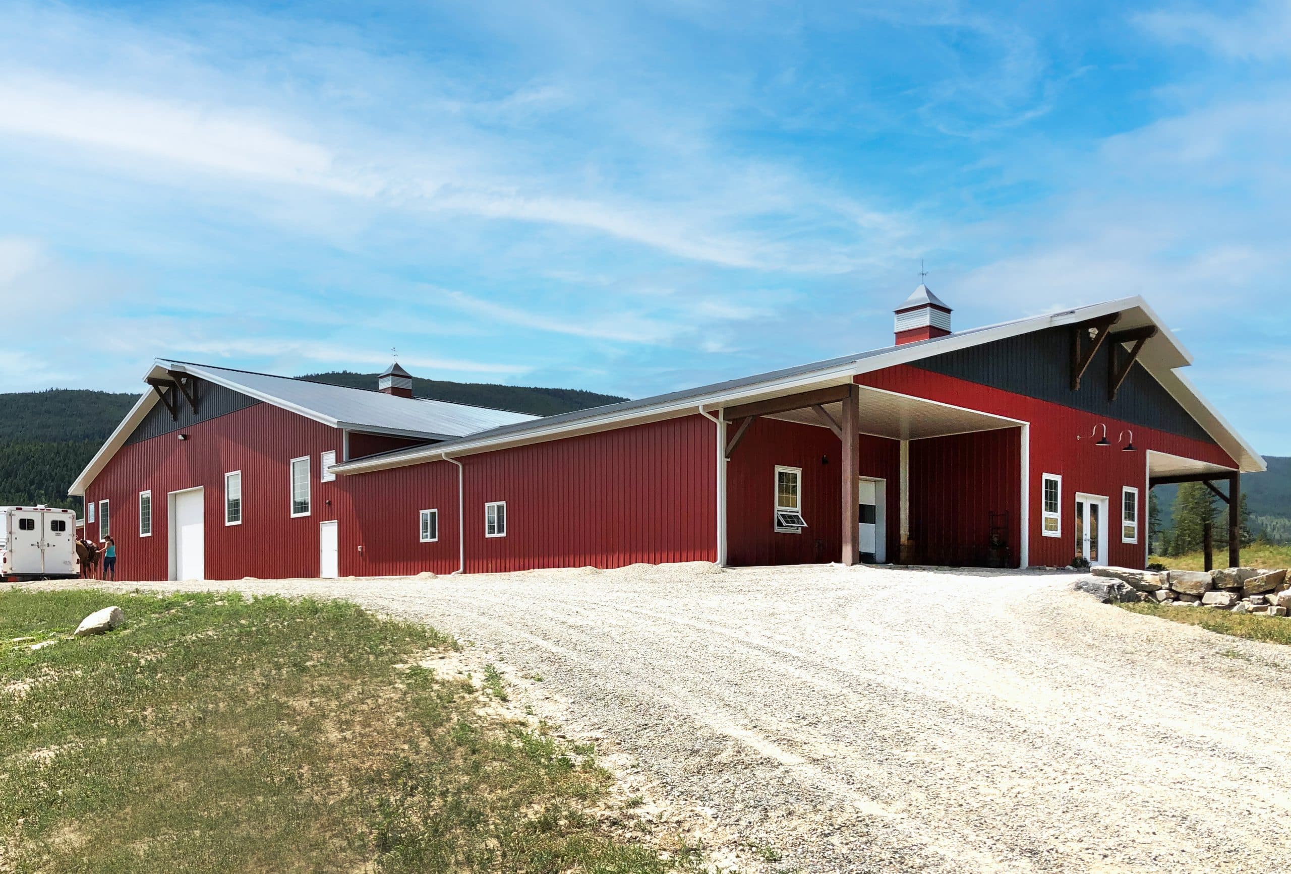 A tile red post-frame riding arena with overhead doors, timber accents, and soffits