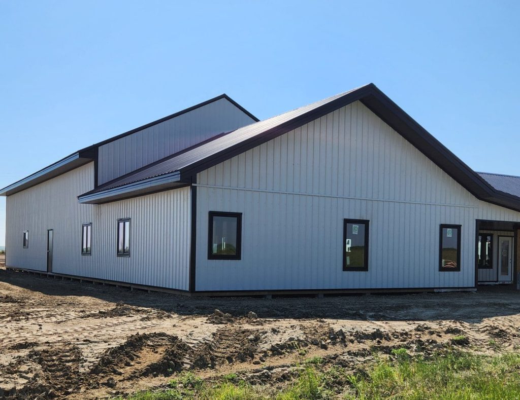 A white white post-frame custom residential build with soffits, open lean-to porch, and overhead doors