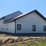 A white white post-frame custom residential build with soffits, open lean-to porch, and overhead doors