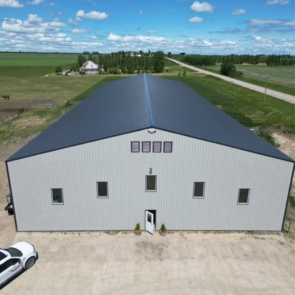 A stone grey post-frame riding arena with three overhead doors