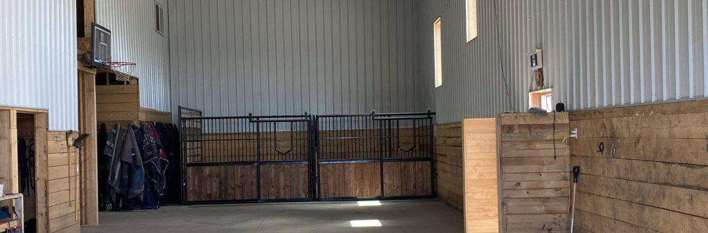 A stone grey post-frame riding arena with three overhead doors