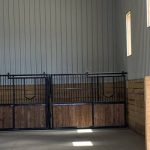 A stone grey post-frame riding arena with three overhead doors