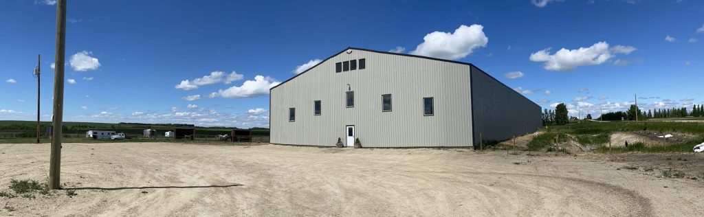 A stone grey post-frame riding arena with three overhead doors